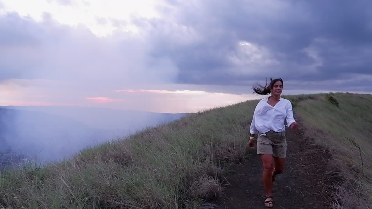 Donna cammina su un sentiero sul bordo di un vulcano, sferzata da forte vento in vetta