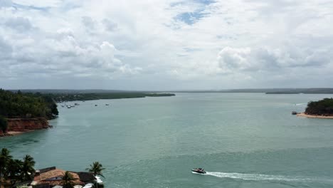 Lowering-aerial-drone-wide-shot-of-a-motorboat-sailing-on-the-huge-tropical-Guaraíras-Lagoon-in-the-famous-beach-town-of-Tibau-do-Sul-near-Pipa,-Brazil-in-Rio-Grande-do-Norte-on-a-cloudy-summer-day