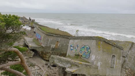 aerial establishing view of abandoned seaside fortification buildings at karosta northern forts, baltic sea coast , large waves, overcast day, slow motion, drone shot moving forward