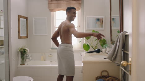 happy african american man dancing shirtless in bathroom looking in mirror having fun morning routine getting ready enjoying positive self image doing silly dance celebrating success