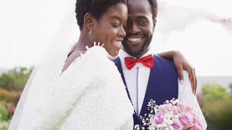 Happy-african-american-couple-embracing-and-smiling-during-wedding