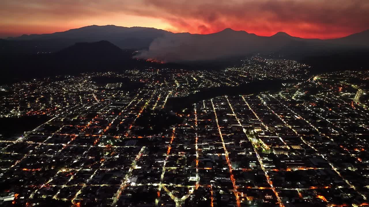 Aerial View of City at Night with Distant Wildfire and Red Sky