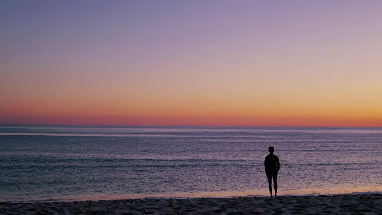 Silhouette of a person sitting on a beach at sunset, captured from a side angle