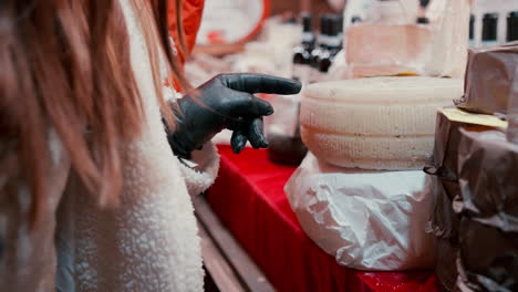 mujer apuntando a un queso con su dedo y midiendo el grosor usando guantes negros y abrigo blanco