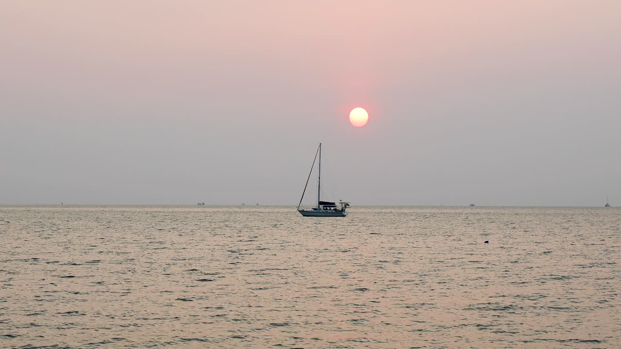 Amazing Sunset with the Sun Going Down Over the Horizon with a Yacht in Silhouette in Bangsaray near Pattaya, Thailand. Stationary Medium Zoomed Shot in 4K