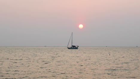 amazing sunset with the sun going down over the horizon with a yacht in silhouette in bangsaray near pattaya, thailand. stationary medium zoomed shot in 4k