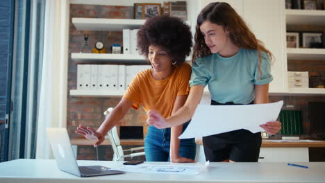 two female architects with laptop meeting and discussing building plans in modern office