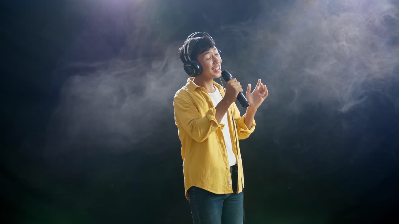 헤드폰을 들고 마이크를 들고  연기 검은 바탕에 노래하는 아시아 소년