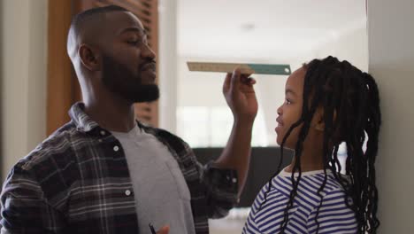 Happy-african-american-father-measuring-his-daughter-at-home