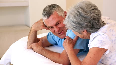 Happy-senior-couple-lying-on-bed-chatting