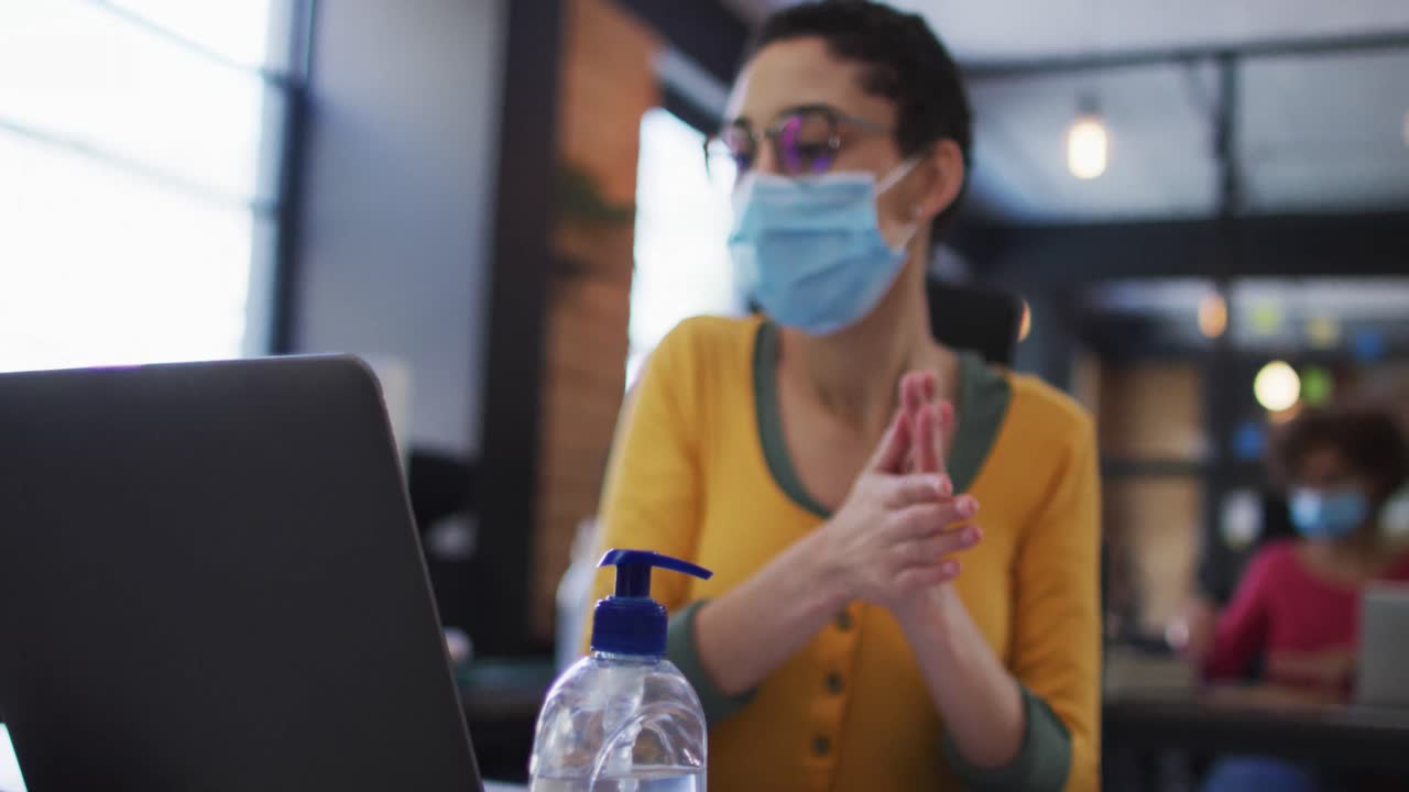 mujer caucásica con máscara facial usando desinfectante de manos en una oficina moderna