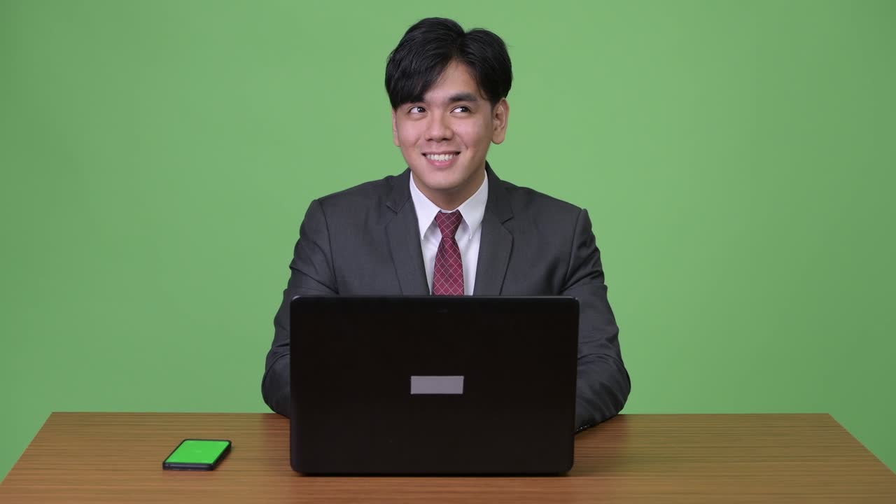 젊은 잘생긴 아시아 사업가가 초록색 배경에 노트북을 가지고 일하고 있습니다.