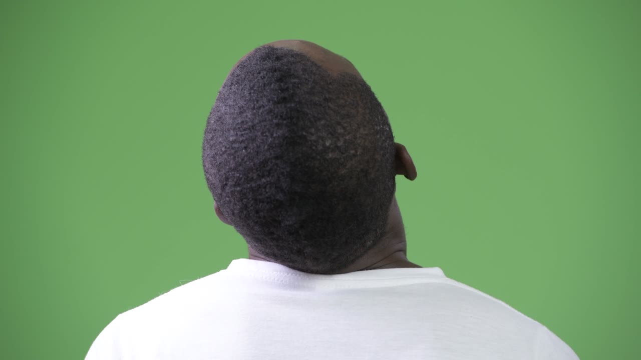 Rear view of young African man with neck pain against green background