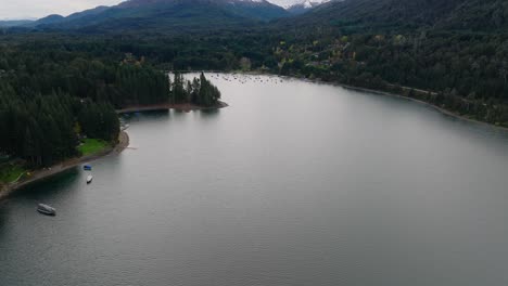 aerial flying over nahuel huapi lake at san carlos de bariloche with tilt up reveal of snow capped mountain in background