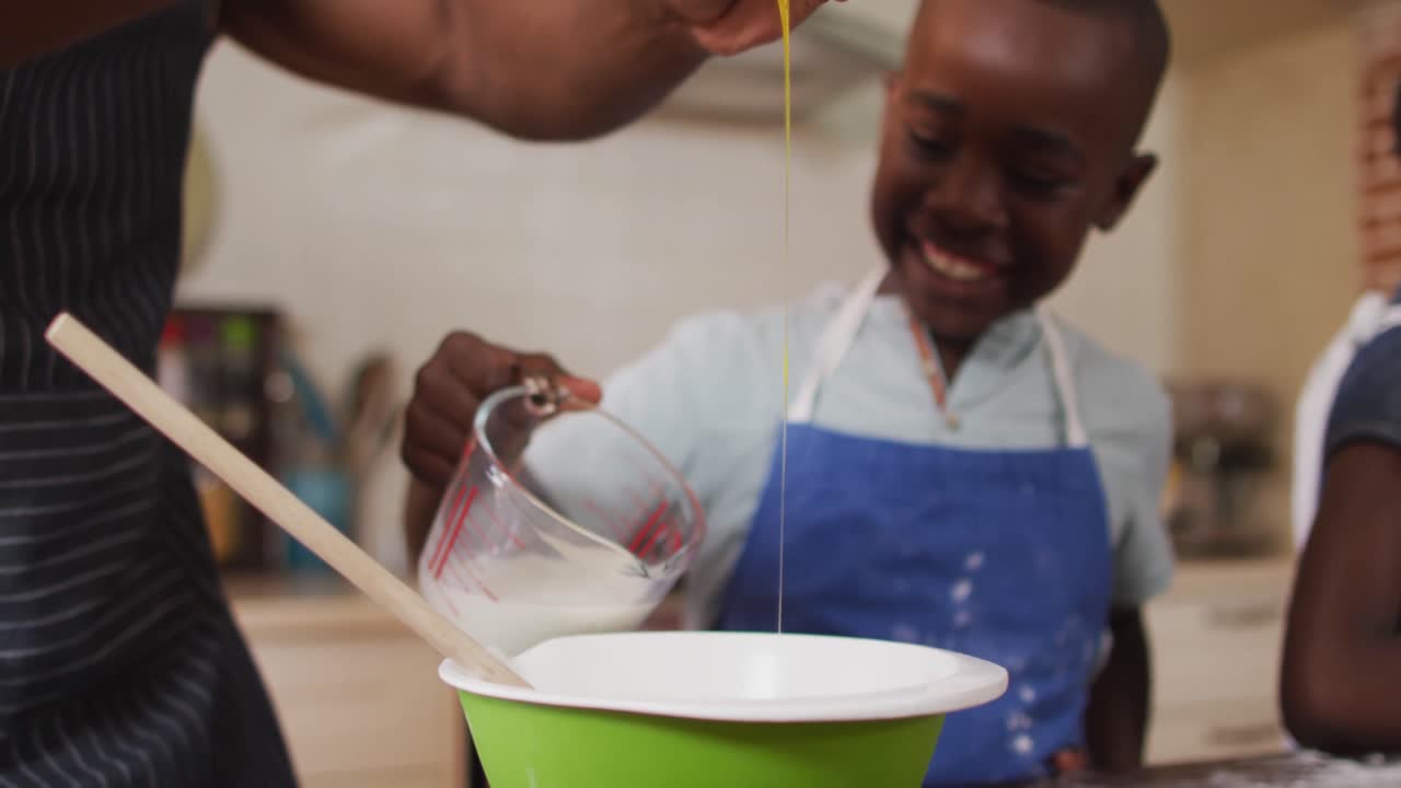 African american father and son wearing aprons baking together in the kitchen at home