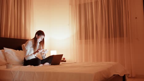 beautiful woman lying on bed doing shopping online with credit card. girl sitting on her bed with laptop, having online shopping, keying in credit card. student making purchase via internet