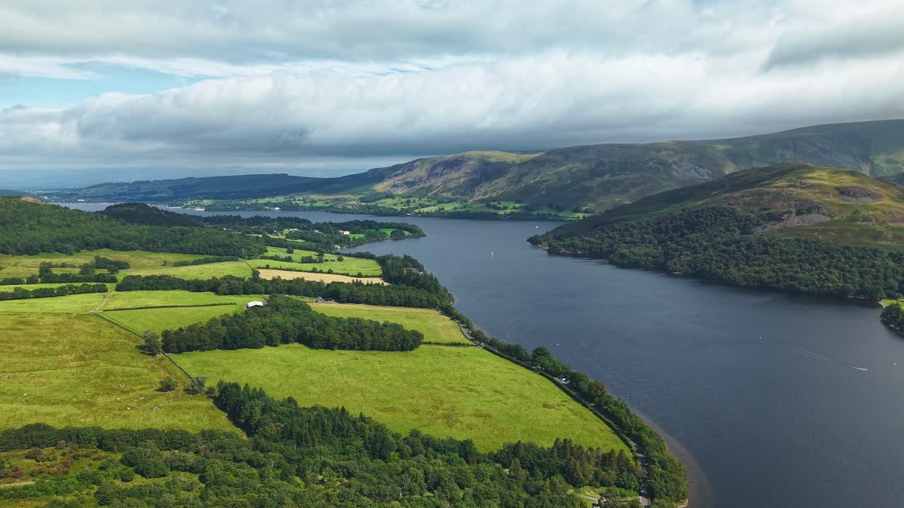 Aerial drone footage flying along Ullswater lake with fells and green fields in summer