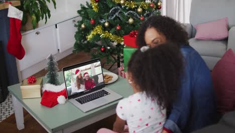 African-american-mother-and-daughter-on-video-call-with-female-friend-and-daughter-at-christmas-time