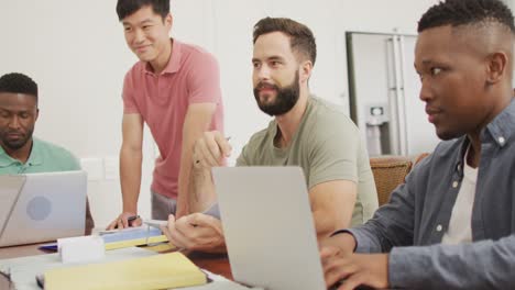 Happy-diverse-male-friends-talking-and-using-laptop-in-living-room