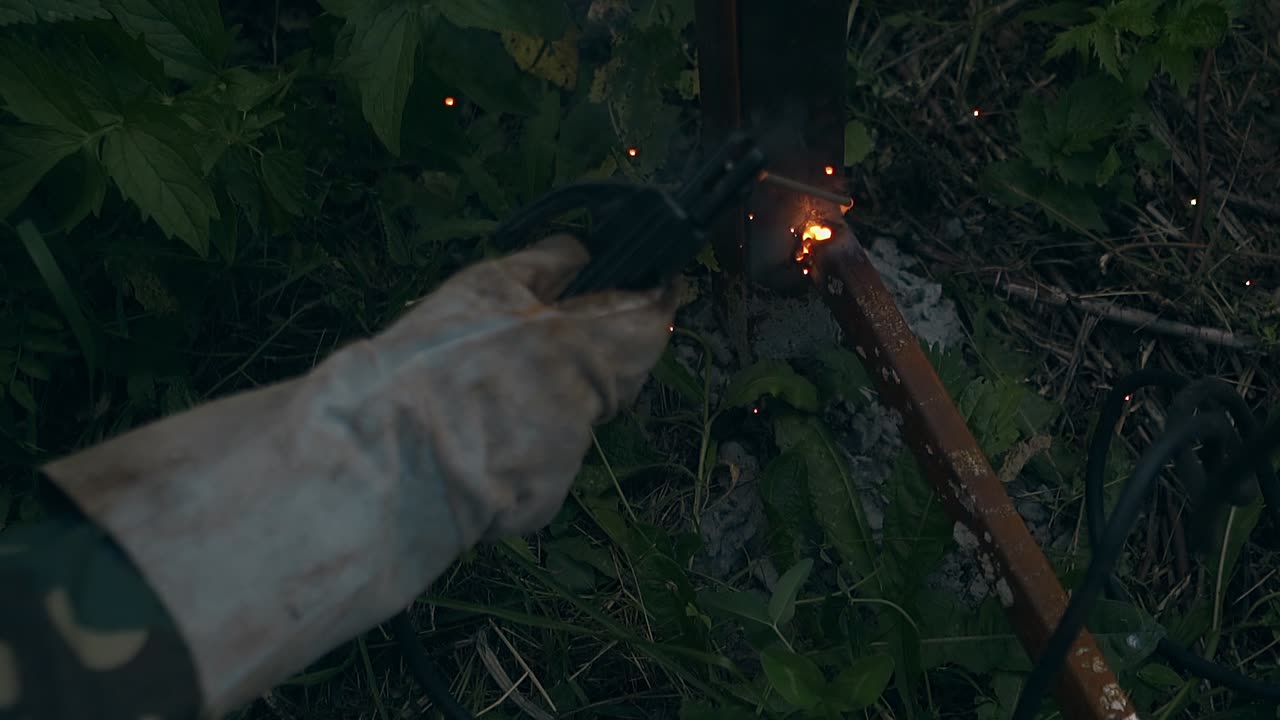 장갑을 입은 느린 클로즈업 노동자가 울타리에 판을 용접합니다.