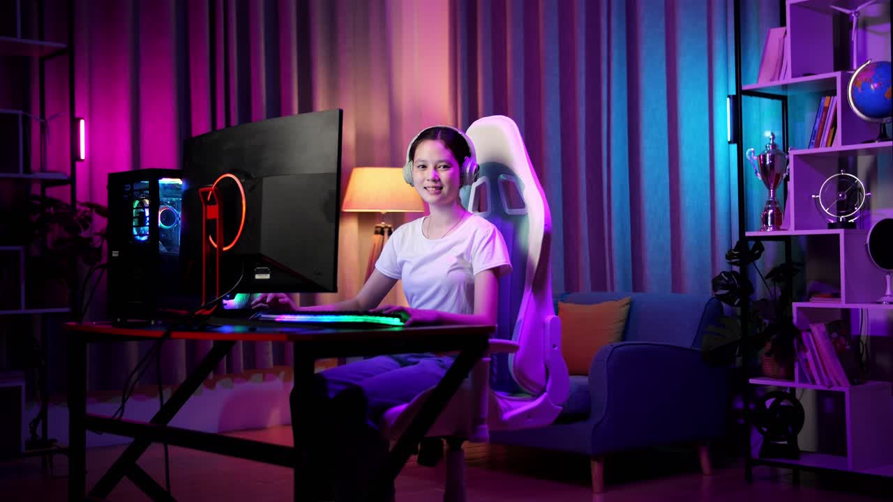 una adolescente asiática sonriendo a la cámara y mostrando el pulgar hacia arriba mientras juega videojuegos en la computadora