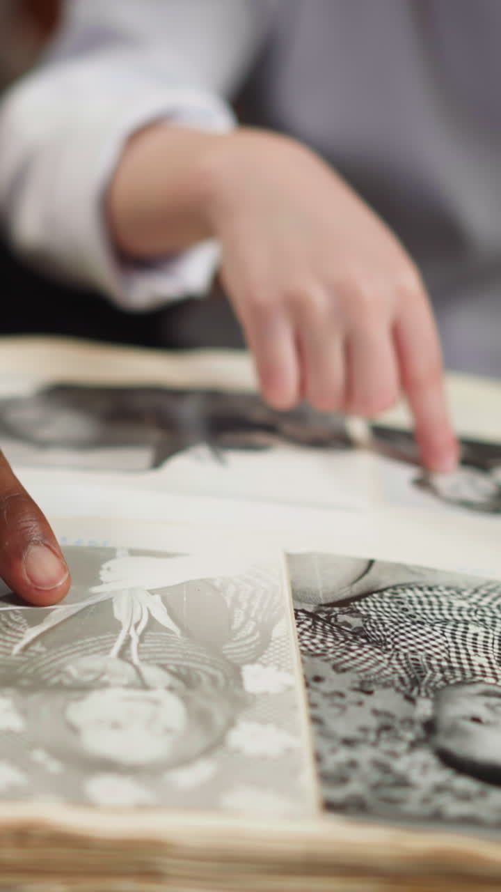 Little white daughter with black step father recall family history looking at pictures in old family photo album at table closeup slow motion