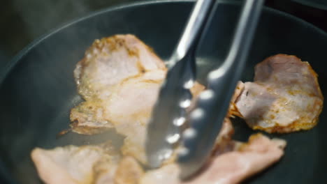 grilling ham slices in a black pan, flipped with metal tongs