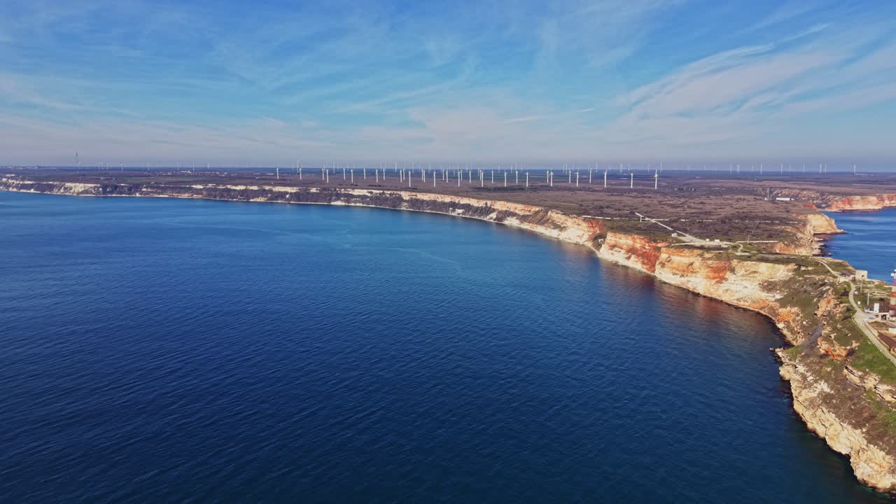 Costa con scogliere e turbine eoliche sotto un cielo blu