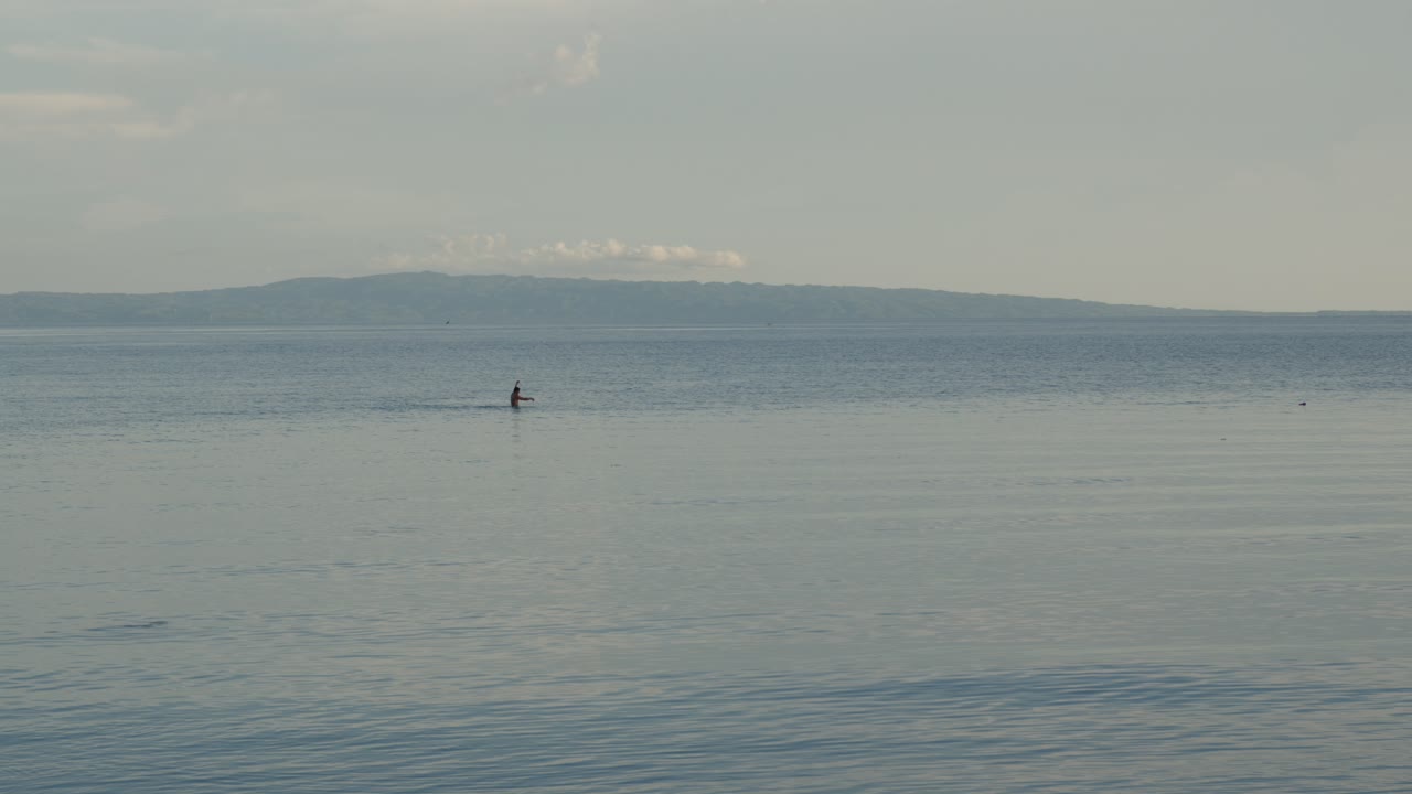 Abitante di un villaggio nelle Filippine che pesca nell'oceano con montagne sullo sfondo all'alba.