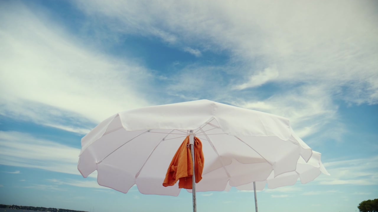 Ombrellone da spiaggia bianco che offre ombra e comfort sotto un cielo azzurro brillante, a simboleggiare il relax e il tempo libero estivo