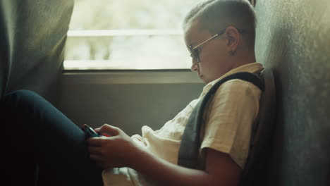 school boy using gadget playing games in school bus. child sitting at bus window