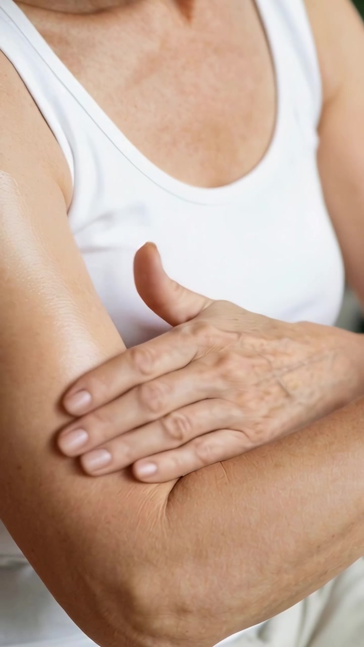 Video verticale: Applicazione di una striscia di crema, persona anziana che si strofina la parte superiore del braccio sinistro per la cura della pelle a casa, con canotta bianca