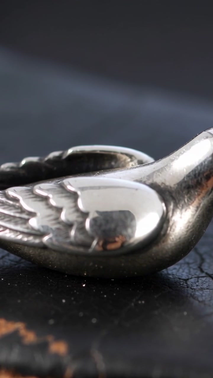 Vertical video: Panning camera revealing silver bird pendant on scuffed black surface, showing wing