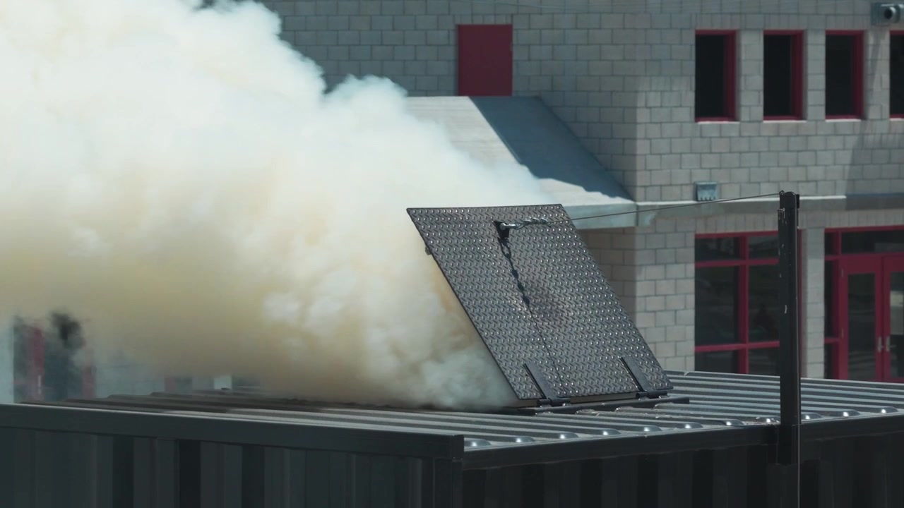 Aerial telephoto close-up shot of thick smoke venting out of a flashover training module during a live-fire exercise in Ventura County, California. 4K