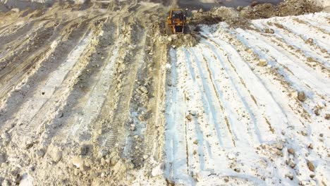 aerial view of bulldozer pushing snowy soil after blizzard in canada