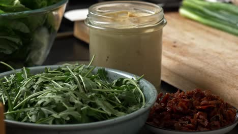fresh ingredients for a vegetable wrap sit ready in containers with hands placing green onions in a bowl