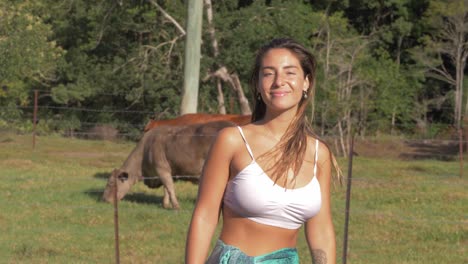 sexy caucasian woman looking at cows eating on pasture turn around and smile at camera - rural farm at currumbin valley, qld, australia