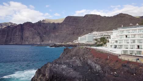 Vista-Aérea-De-La-Costa-De-La-Isla-De-Tenerife-Con-Resort-De-Playa-En-El-Acantilado-Y-Vista-De-Los-Gigantes,-Isla-Canaria-España