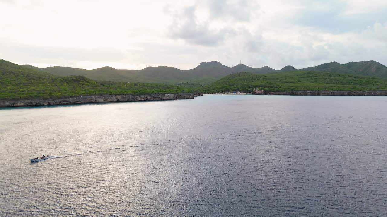 Aerial drone establishing overview of peaceful tropical bay at Kenepa Grande , capturing lush green hills surrounding the calm turquoise waters of the Caribbean
