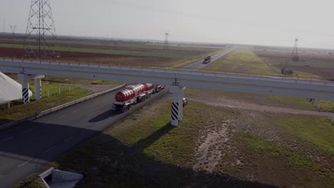 Trailers-on-asphalt-road-in-Reynosa,-Tamaulipas,-Mexico-with-a-bridge-on-a-sunny-day,-drone-shot-4k