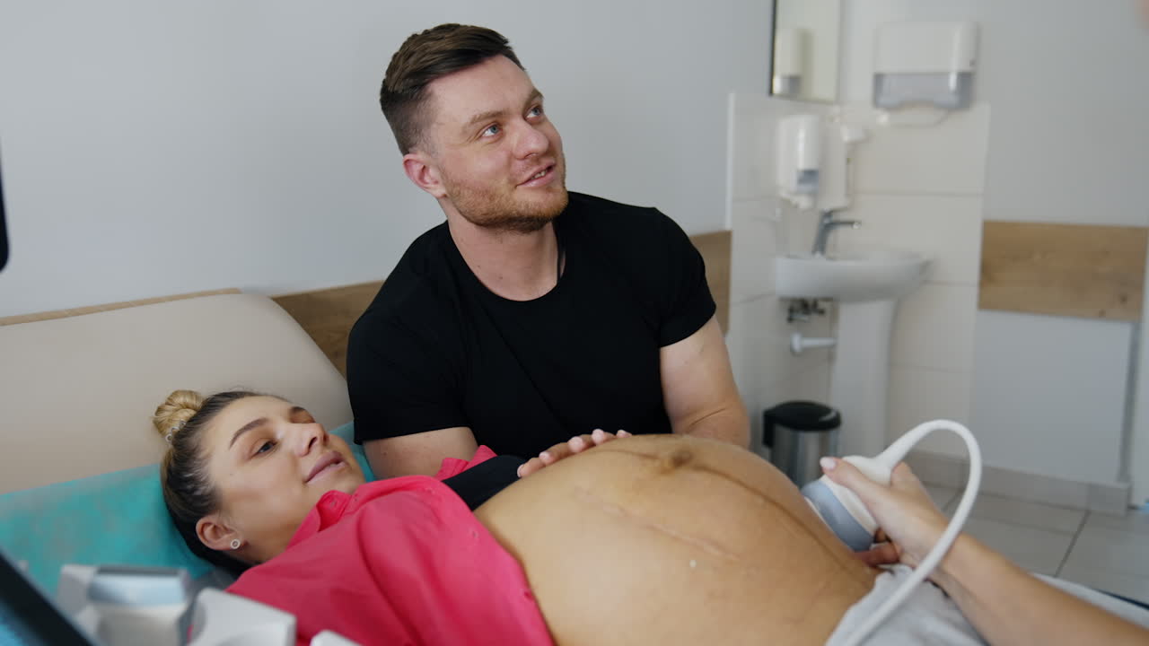Expecting couple talk and smile to each other in the doctor's cabinet. Happy future parents at pregnancy check up.