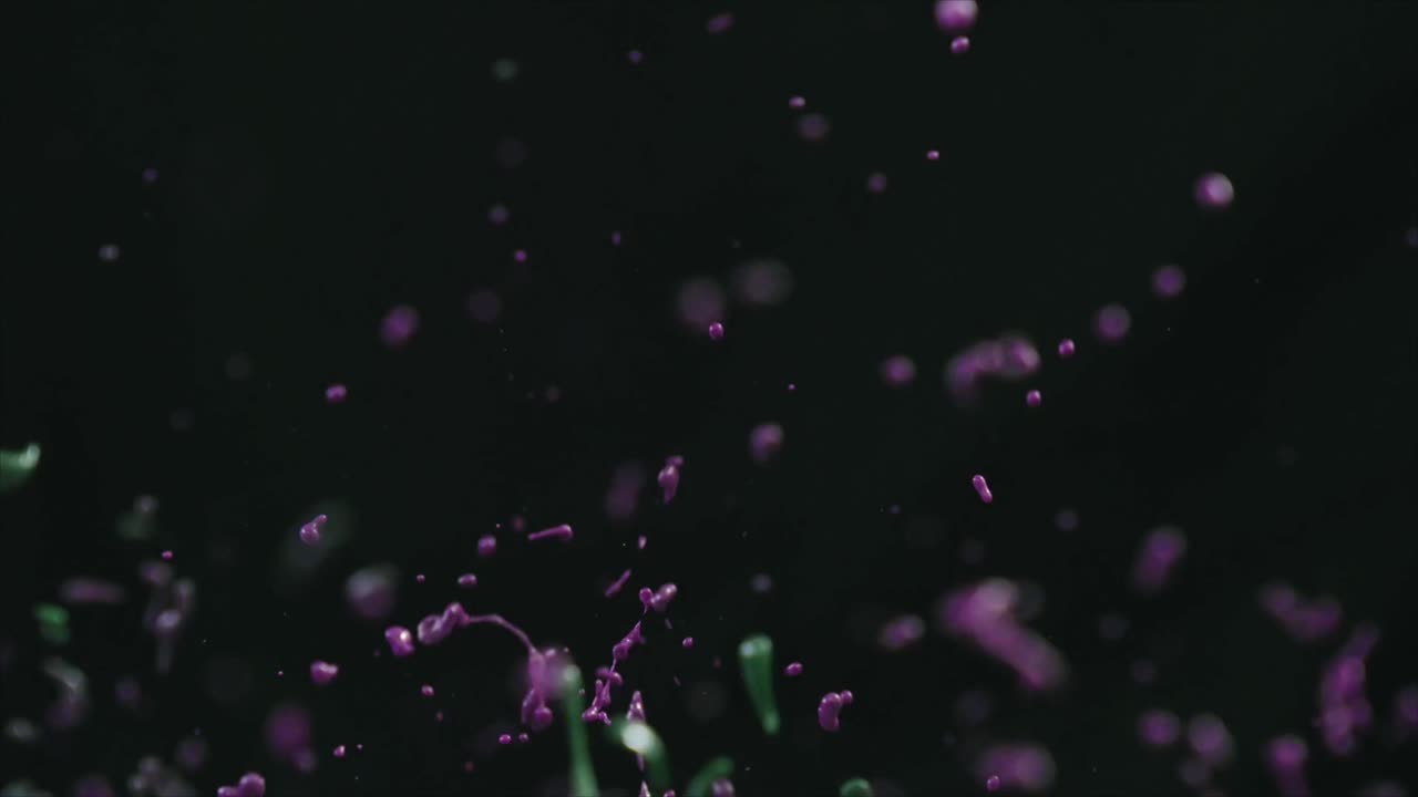 Lilla og grønne væskestænk på mørk baggrund i slow motion