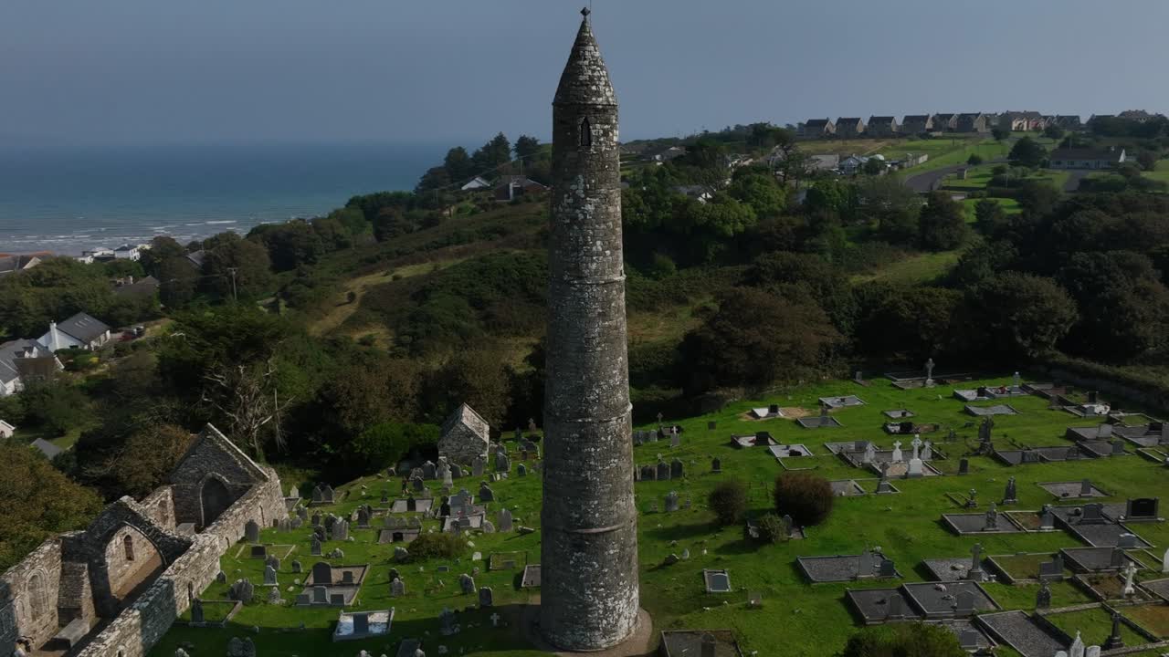 St. Declan's Monastery, Ardmore, County Waterford, Ireland, September 2024. Drone orbits counter clockwise ascending around the Round Tower and cemetery with ocean views stretching to the horizon.