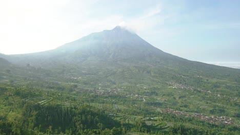 vuelo aéreo lento hacia adelante sobre plantaciones rurales con volcán merapi en segundo plano