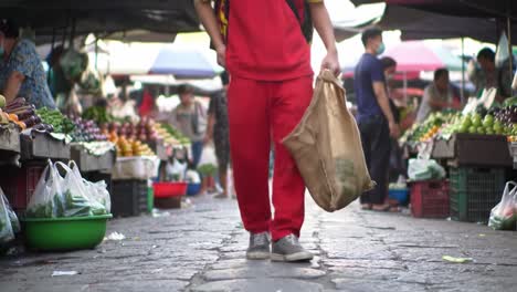 a person in a red outfit walks through a lively market filled with fresh produce and customers enjoying their shopping experience. the atmosphere is full of energy and various colors.