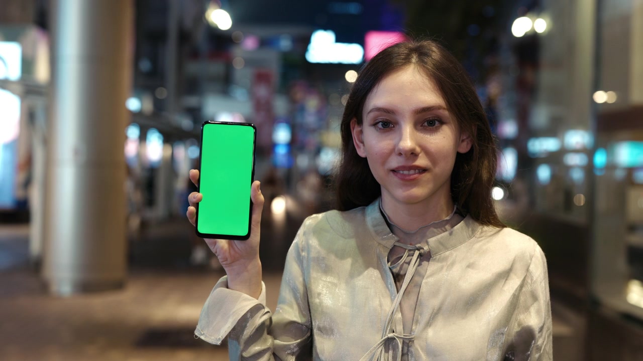 Giovane donna con smartphone a schermo verde che sorride alla fotocamera
