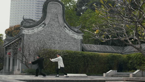 two men practice tai chi in a traditional chinese garden with a modern cityscape in the background