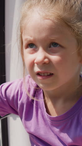 little girl in purple t-shirt disgusted of bright sun shining on face rides glass wall gondola of safe poma lift at mountain resort closeup slow motion