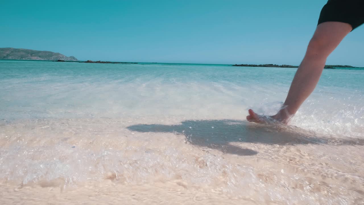 hombre caminando en la playa rosa, pies en el agua