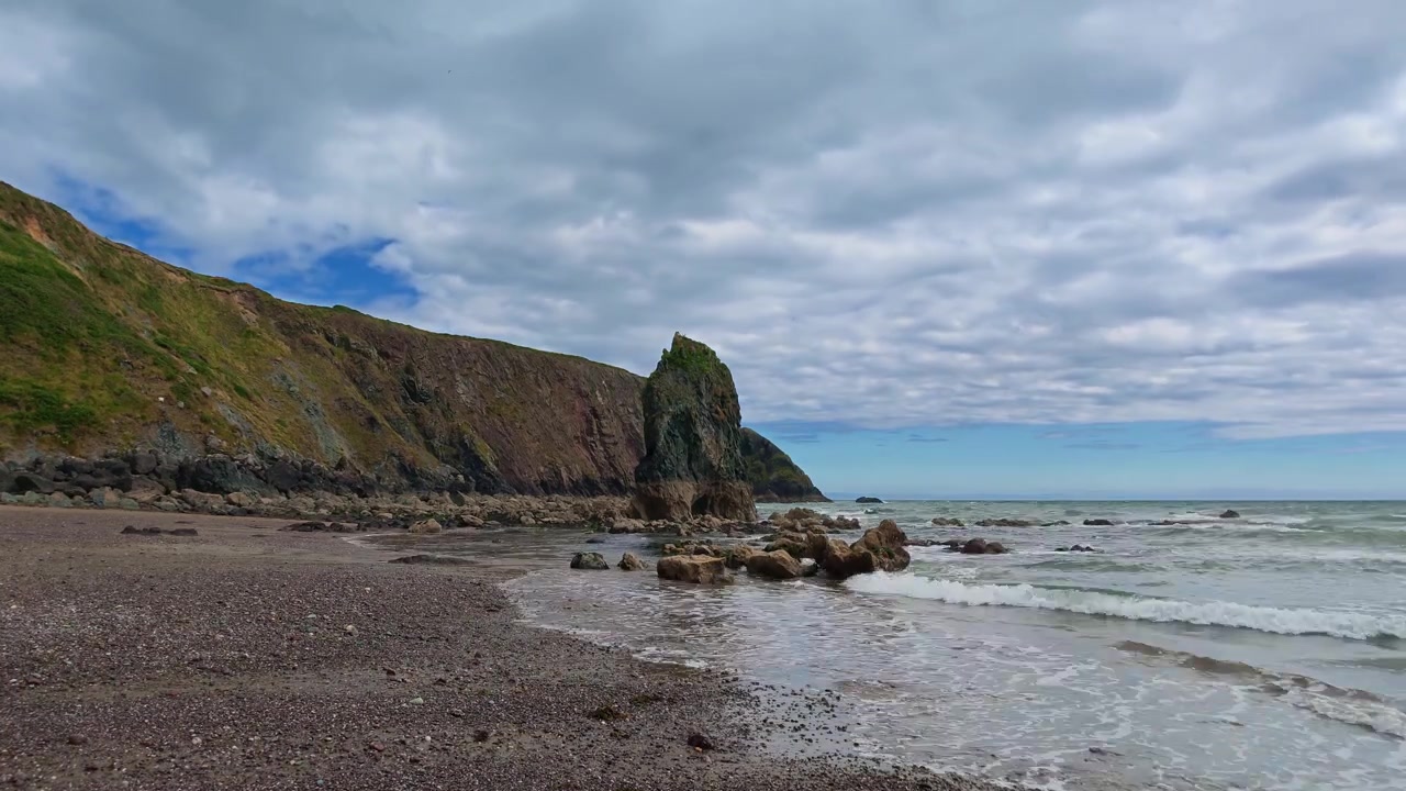Yazın yükselen gelgitlerle korunaklı bir koyda tek bir deniz kayasının bulunduğu Copper Coast, Waterford, İrlanda'dan hızlandırılmış çekim.
